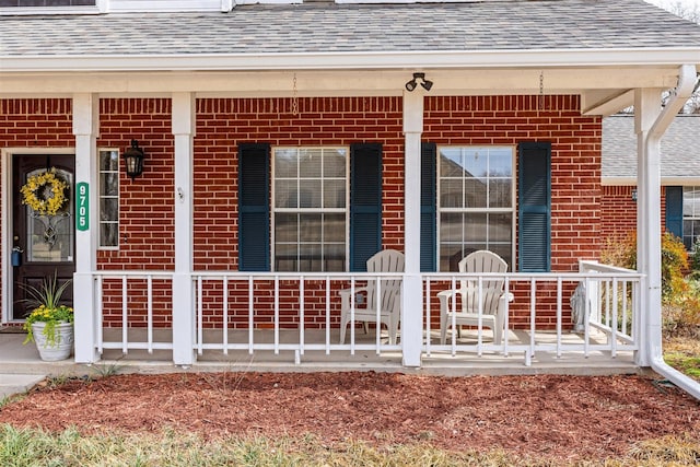 view of exterior entry featuring a porch, brick siding, and a shingled roof