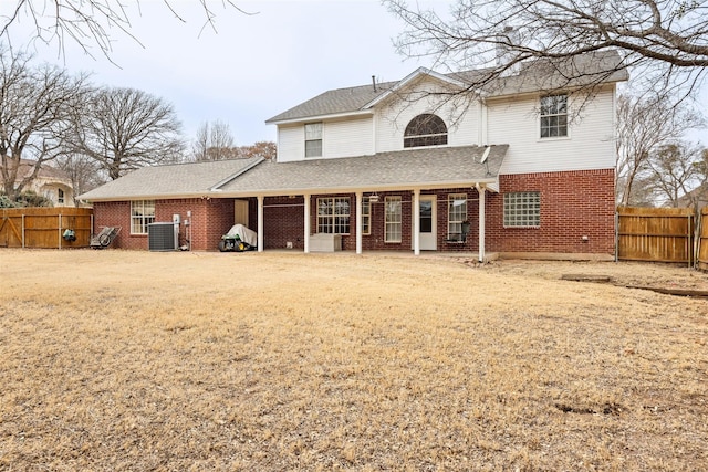 rear view of property featuring brick siding, roof with shingles, central AC unit, and fence