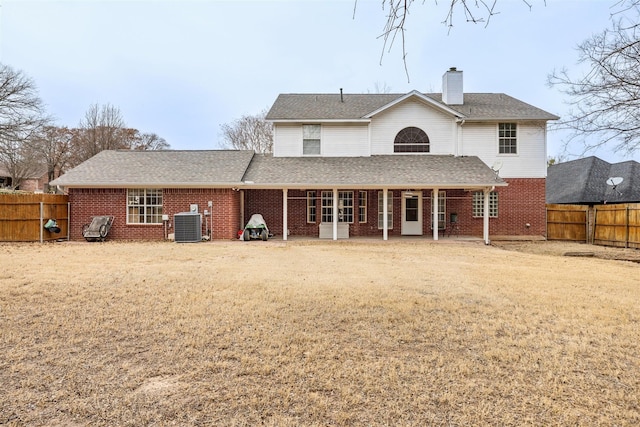 rear view of property featuring central air condition unit, a fenced backyard, a chimney, and brick siding