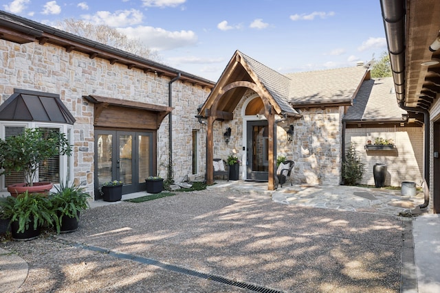 exterior space featuring stone siding, roof with shingles, a patio, and french doors