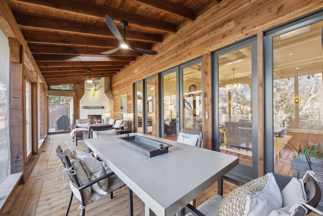 sunroom / solarium featuring lofted ceiling with beams, wood ceiling, an outdoor stone fireplace, and ceiling fan with notable chandelier