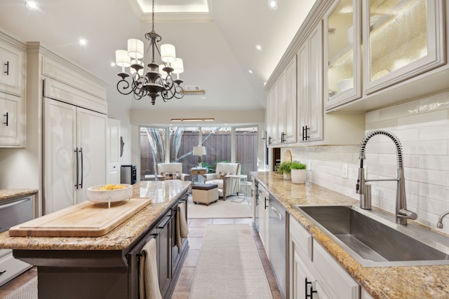 kitchen featuring light stone counters, stainless steel dishwasher, glass insert cabinets, a sink, and paneled built in refrigerator