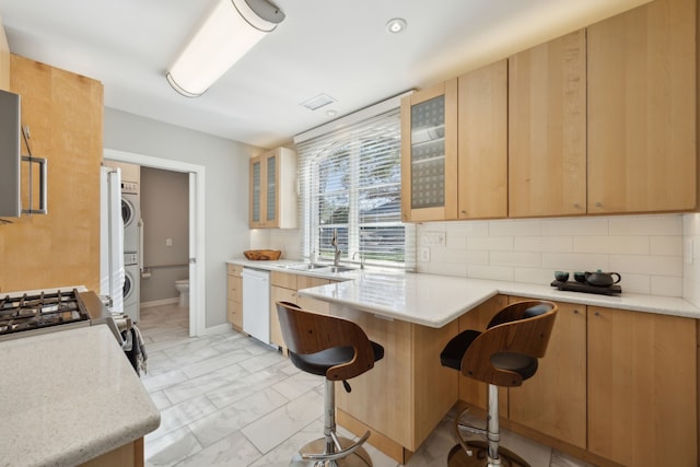 kitchen featuring decorative backsplash, stacked washer / drying machine, marble finish floor, white dishwasher, and a sink