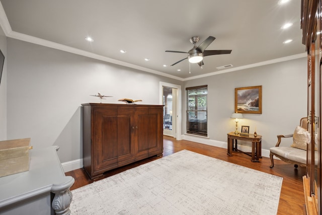 living area featuring baseboards, visible vents, a ceiling fan, ornamental molding, and wood finished floors