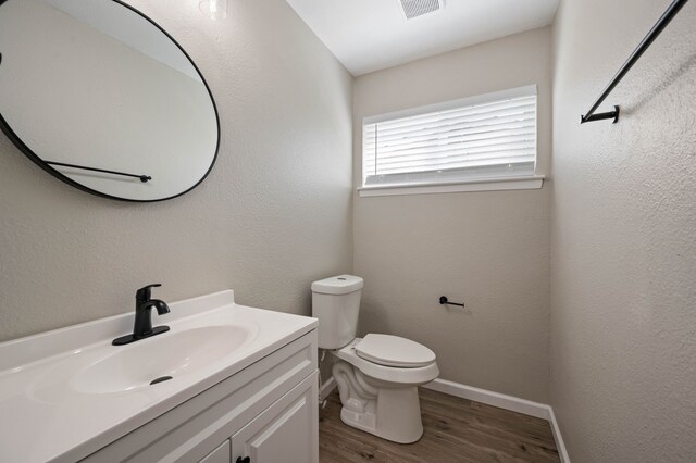 bathroom featuring visible vents, baseboards, toilet, wood finished floors, and vanity