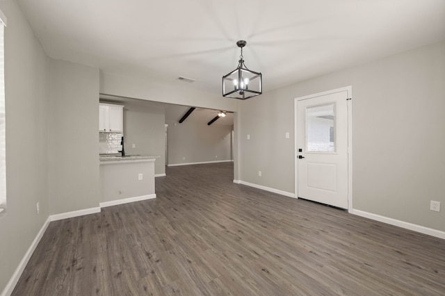 unfurnished living room with dark wood-type flooring, visible vents, a notable chandelier, and baseboards