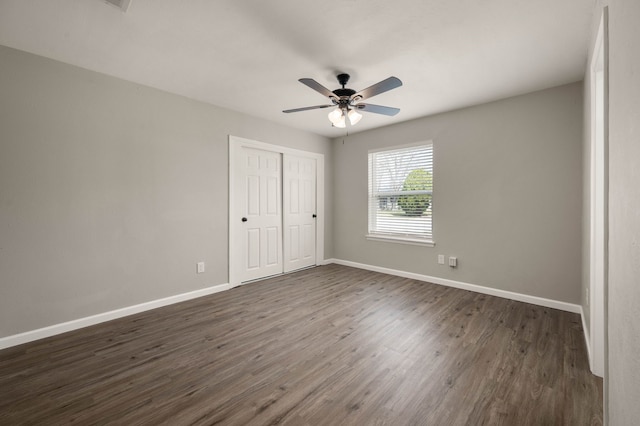 unfurnished bedroom featuring a closet, dark wood finished floors, baseboards, and ceiling fan