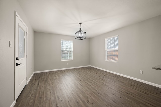 spare room with dark wood-style floors, baseboards, and a notable chandelier