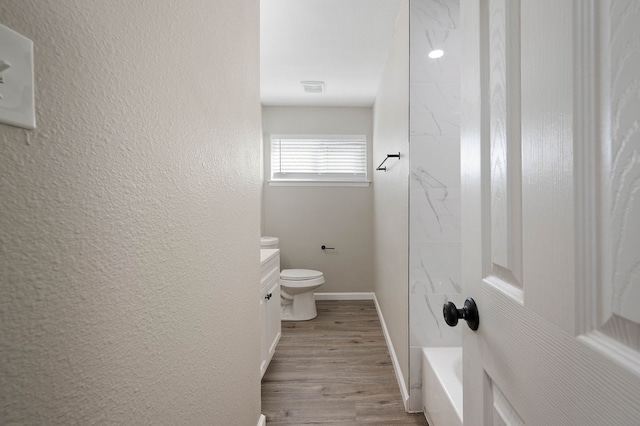 full bath featuring a textured wall, toilet, vanity, wood finished floors, and baseboards