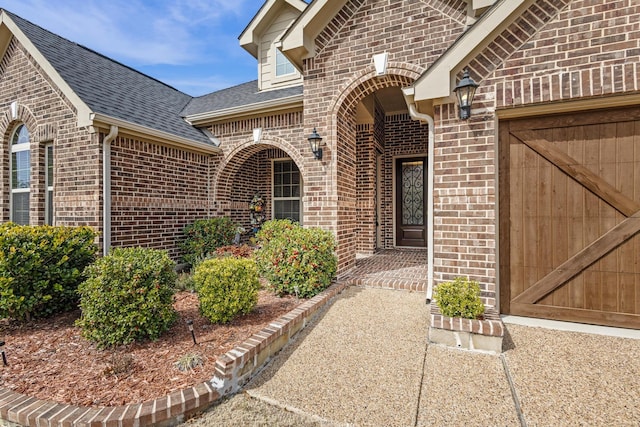 property entrance featuring a garage, roof with shingles, and brick siding