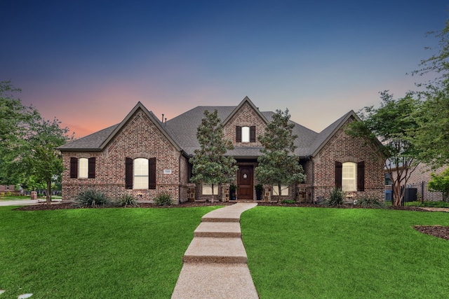 french country style house featuring brick siding, a yard, and roof with shingles