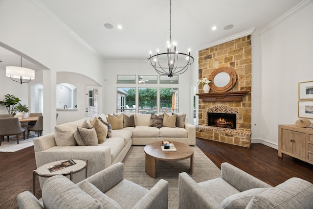 living area with arched walkways, dark wood-style flooring, a fireplace, crown molding, and a towering ceiling