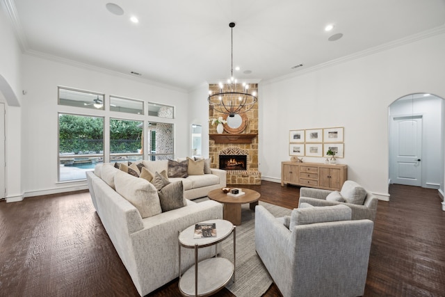 living room featuring arched walkways, a stone fireplace, visible vents, ornamental molding, and dark wood-style floors