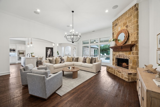 living area with arched walkways, dark wood finished floors, ornamental molding, a stone fireplace, and a chandelier