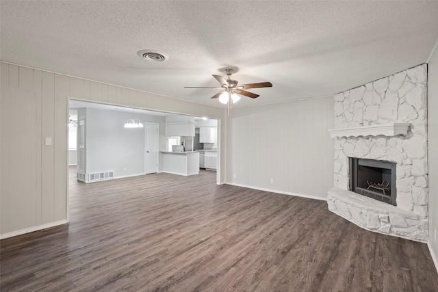 unfurnished living room with dark wood-type flooring, a fireplace, visible vents, and a ceiling fan