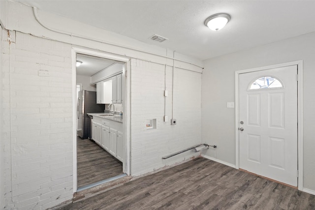 interior space with dark wood-style flooring, visible vents, a sink, and brick wall