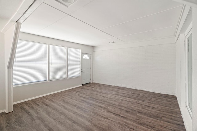 unfurnished room featuring brick wall and wood finished floors