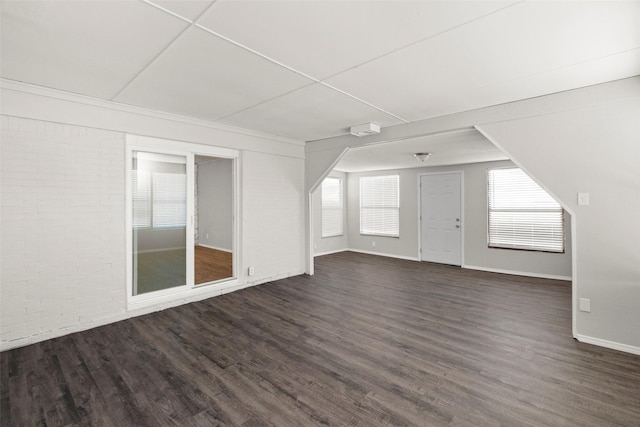 bonus room featuring dark wood-type flooring, baseboards, and brick wall