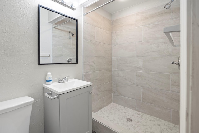 full bathroom featuring toilet, a textured wall, a tile shower, and vanity