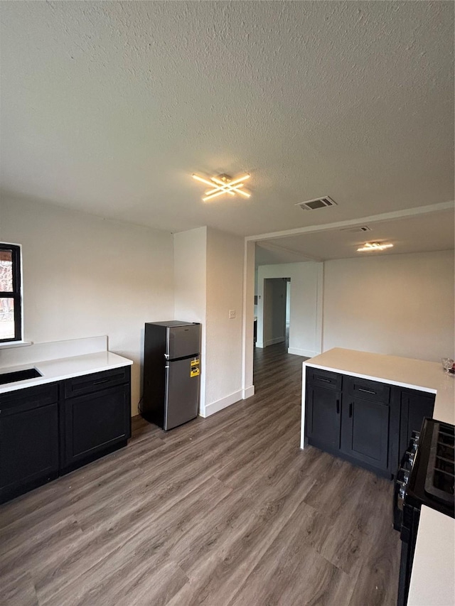 kitchen with light wood finished floors, light countertops, visible vents, freestanding refrigerator, and dark cabinets