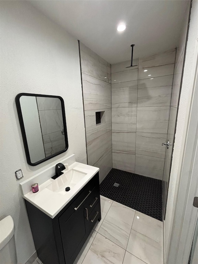 bathroom with marble finish floor, tiled shower, vanity, and toilet