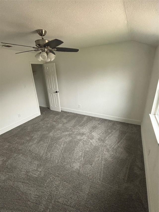 spare room featuring visible vents, dark carpet, vaulted ceiling, a textured ceiling, and ceiling fan