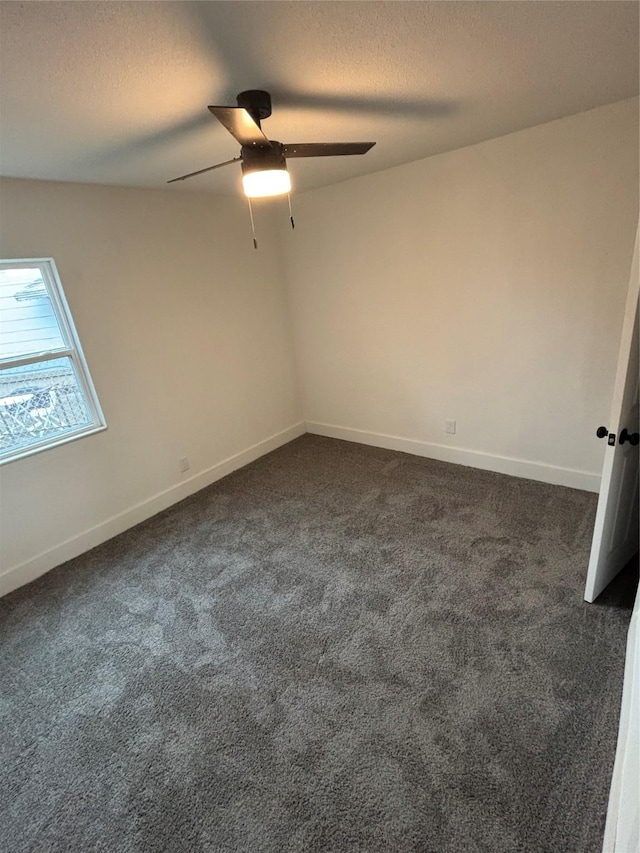 spare room with a textured ceiling, dark colored carpet, ceiling fan, and baseboards