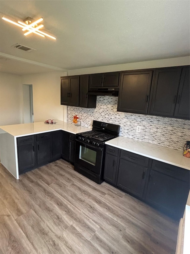 kitchen with under cabinet range hood, a peninsula, visible vents, black range with gas stovetop, and light wood finished floors