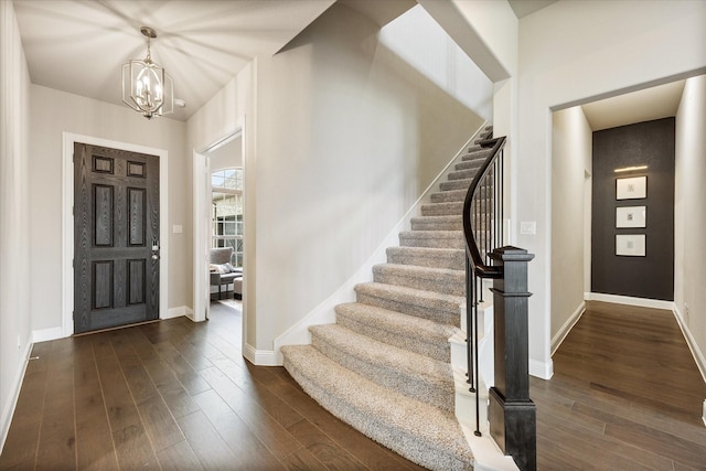 entryway featuring dark wood-type flooring, an inviting chandelier, baseboards, and stairs