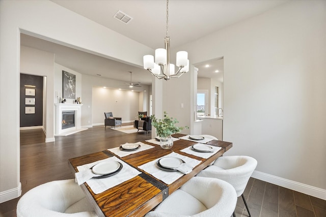 dining area with visible vents, baseboards, a glass covered fireplace, dark wood-style flooring, and a notable chandelier