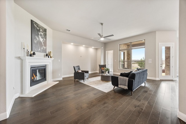 living room with dark wood finished floors, visible vents, a ceiling fan, a glass covered fireplace, and baseboards