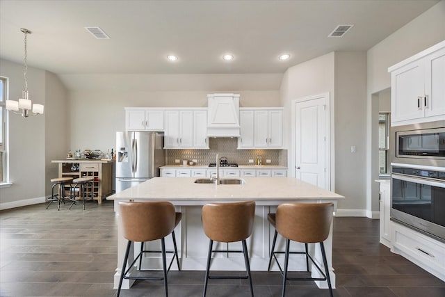 kitchen with premium range hood, visible vents, a kitchen breakfast bar, appliances with stainless steel finishes, and tasteful backsplash