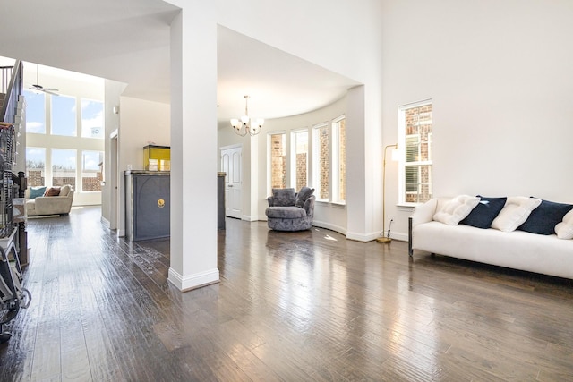 living area with a towering ceiling, plenty of natural light, baseboards, and dark wood-style flooring