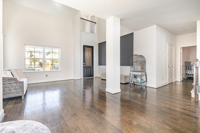 living area featuring ornate columns, a towering ceiling, baseboards, and wood finished floors