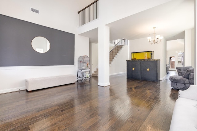 living room with a towering ceiling, an inviting chandelier, stairway, and wood finished floors