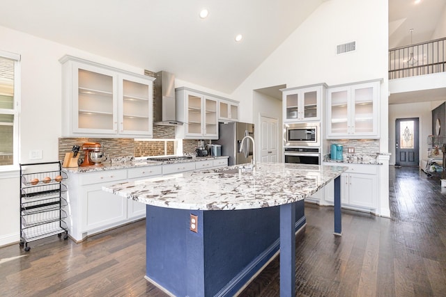 kitchen with stainless steel appliances, dark wood finished floors, an island with sink, and wall chimney exhaust hood