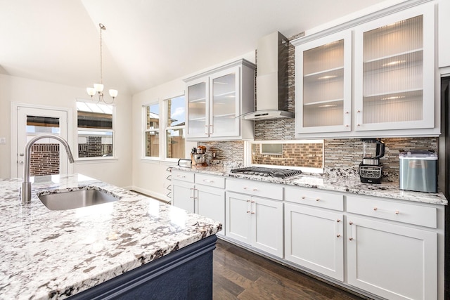 kitchen with wall chimney exhaust hood, backsplash, vaulted ceiling, stainless steel gas cooktop, and a sink