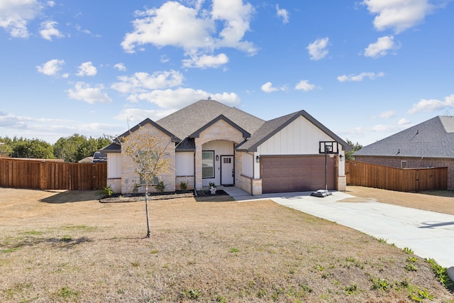 french country home featuring a garage, a shingled roof, concrete driveway, stone siding, and fence