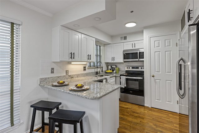 kitchen featuring visible vents, dark wood-style floors, a peninsula, stainless steel appliances, and a sink