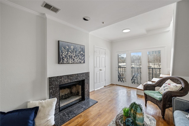 living room featuring visible vents, ornamental molding, wood finished floors, and a high end fireplace