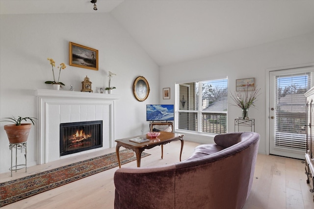 living area with a healthy amount of sunlight, a tiled fireplace, wood finished floors, and lofted ceiling