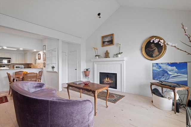 living room featuring high vaulted ceiling, a tile fireplace, and light wood-style floors