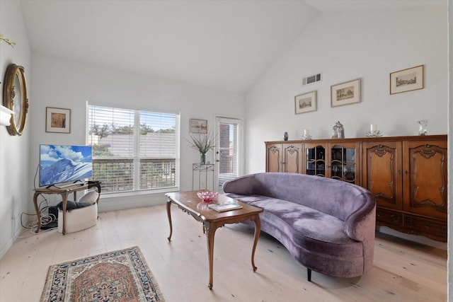 living area with high vaulted ceiling, light wood-type flooring, and visible vents