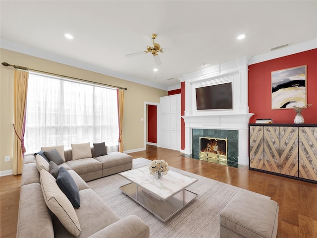 living area featuring wood finished floors, visible vents, baseboards, a high end fireplace, and crown molding