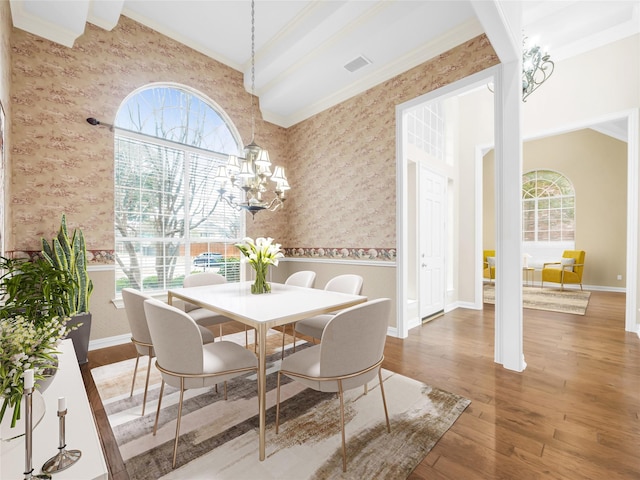 dining space featuring wallpapered walls, ornamental molding, wood finished floors, and an inviting chandelier