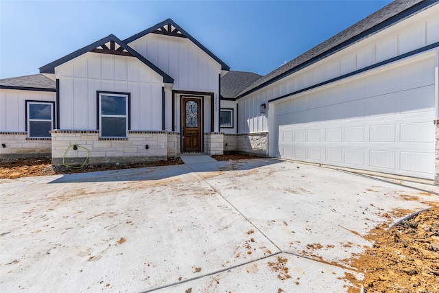 modern inspired farmhouse with driveway, a shingled roof, stone siding, an attached garage, and board and batten siding