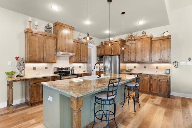 kitchen with stainless steel appliances, a sink, an island with sink, light wood-type flooring, and a kitchen breakfast bar