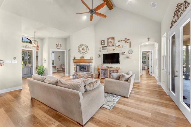 living room featuring arched walkways, a fireplace, visible vents, high vaulted ceiling, and light wood-type flooring