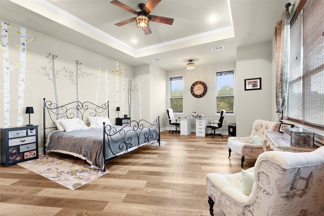 bedroom featuring light wood-style flooring, visible vents, a raised ceiling, and ornamental molding