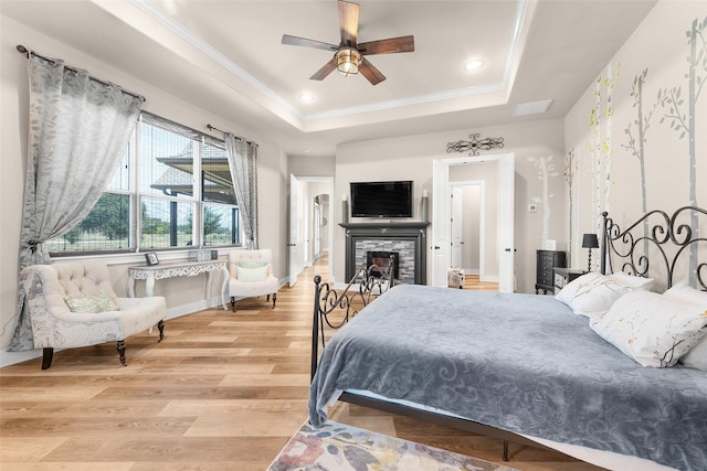 bedroom featuring a tray ceiling, a fireplace, recessed lighting, ornamental molding, and wood finished floors